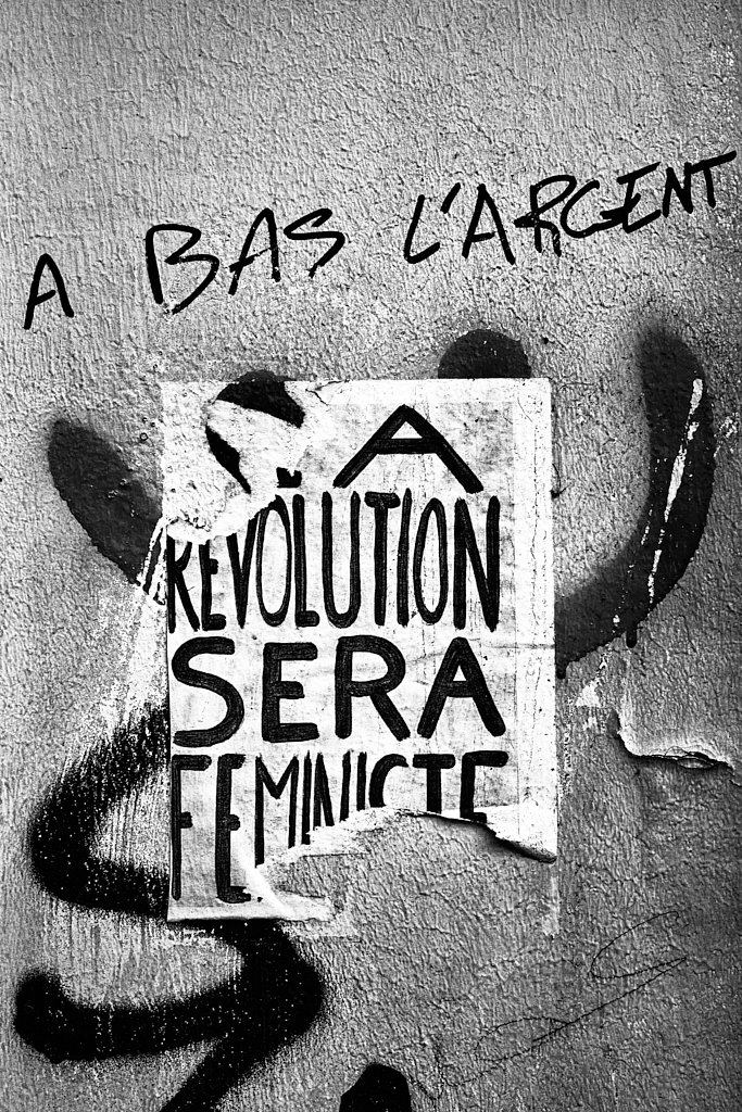 Affiche « La révolution sera féministe » sous le graffiti « À bas l’argent »