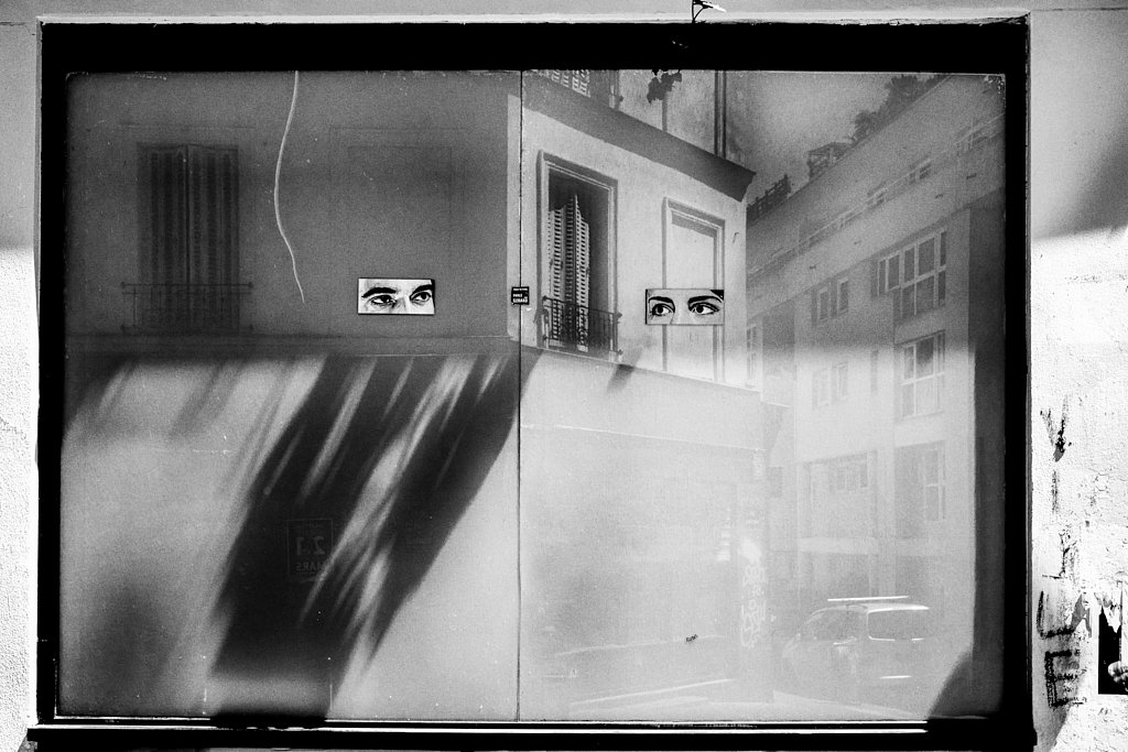 Deux paires d’yeux collées sur une vitrine reflétant la rue