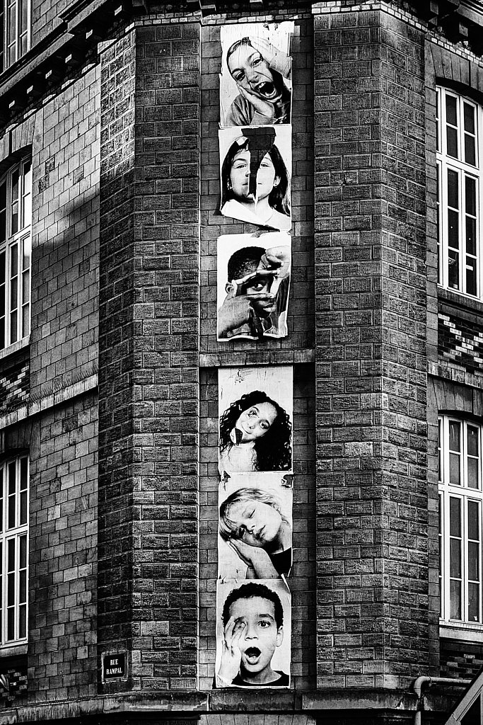 Suite de portraits collés sur la façade à l’angle de la rue Rampal